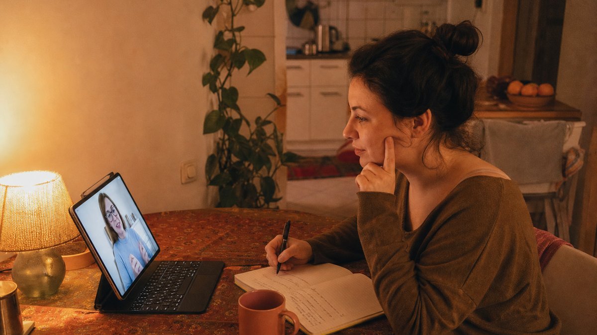 Frau nimmt abends am Küchentisch an einer Online-Sprachstunde mit persönlichem Tutor teil